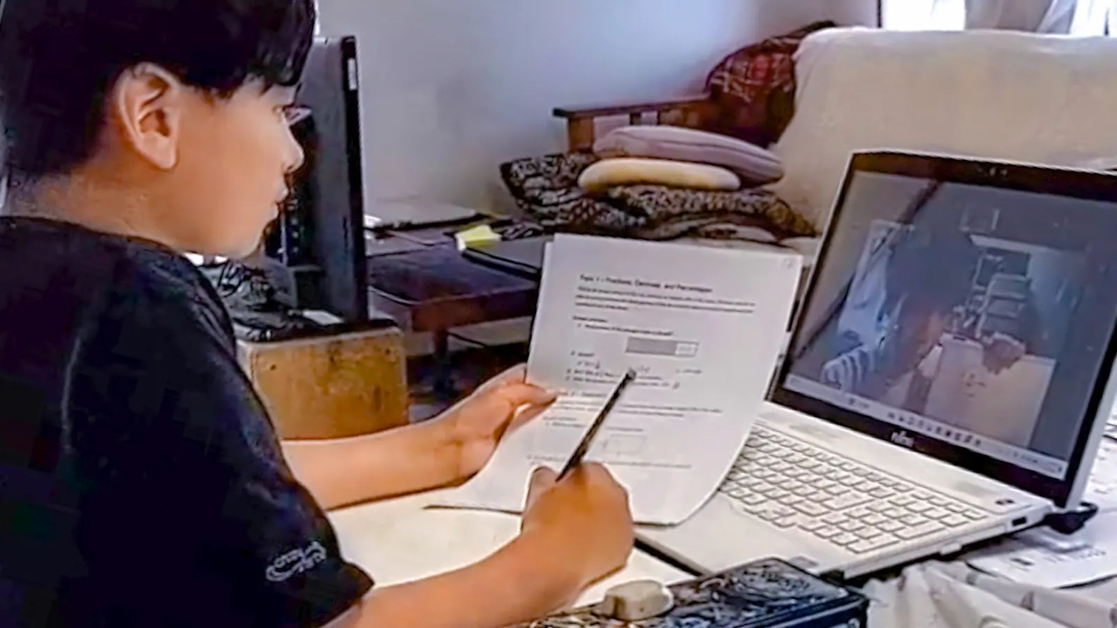 パソコンで英語のオンライン授業を受けながら、ワークシートに英語を書き込んでいる生徒